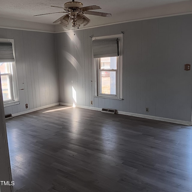 spare room featuring ceiling fan, dark hardwood / wood-style flooring, a textured ceiling, and wooden walls