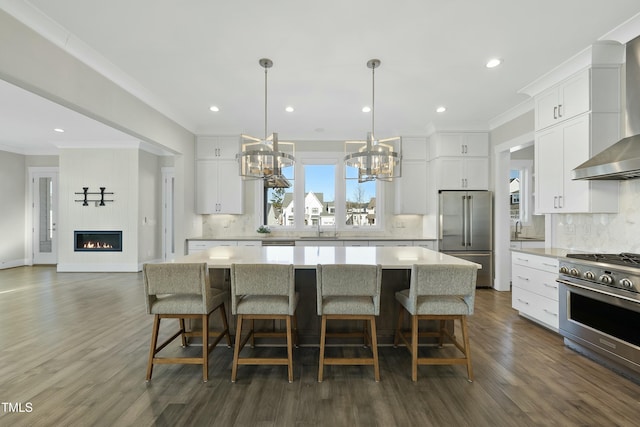 kitchen with wall chimney range hood, a spacious island, decorative light fixtures, white cabinets, and high end appliances