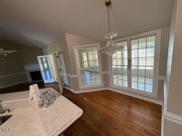 dining area with ceiling fan with notable chandelier, dark hardwood / wood-style flooring, sink, and vaulted ceiling