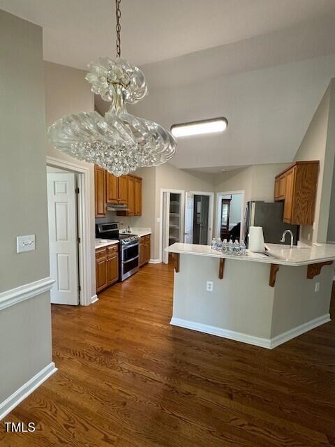 kitchen featuring dark wood-type flooring, appliances with stainless steel finishes, a notable chandelier, kitchen peninsula, and a breakfast bar area