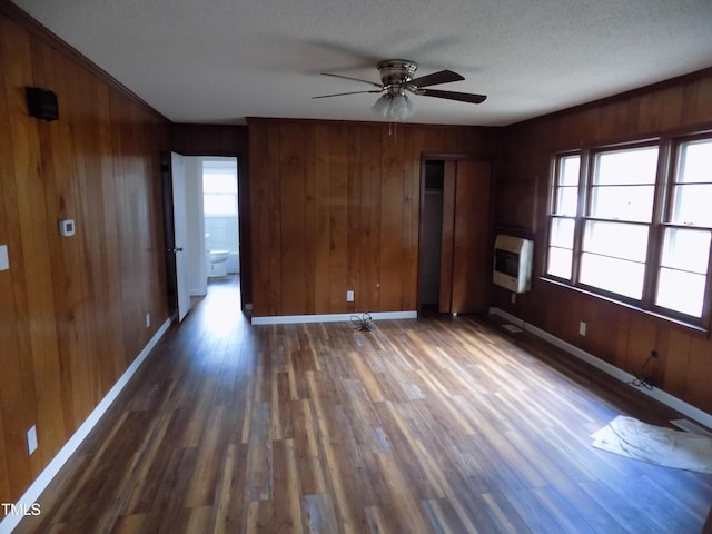 unfurnished room with dark hardwood / wood-style floors, heating unit, wooden walls, and ceiling fan