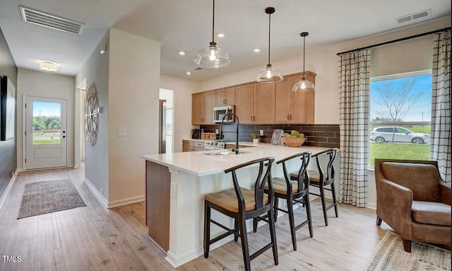 kitchen with light brown cabinetry, tasteful backsplash, sink, decorative light fixtures, and light hardwood / wood-style floors