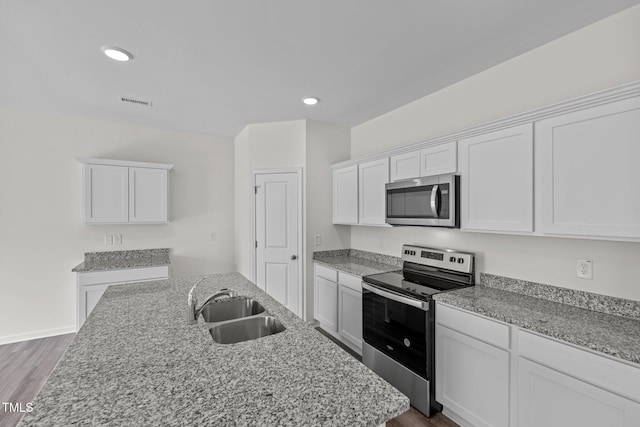 kitchen with light stone countertops, white cabinetry, sink, dark wood-type flooring, and appliances with stainless steel finishes