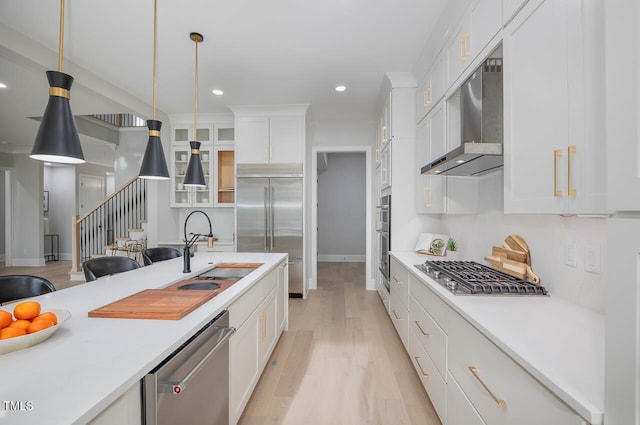 kitchen featuring appliances with stainless steel finishes, wall chimney range hood, pendant lighting, white cabinets, and sink