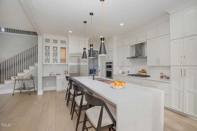 kitchen featuring white cabinetry, wall chimney exhaust hood, a center island with sink, and decorative light fixtures