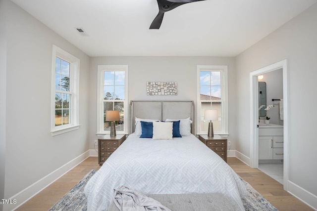 bedroom featuring ceiling fan, multiple windows, ensuite bathroom, and light wood-type flooring