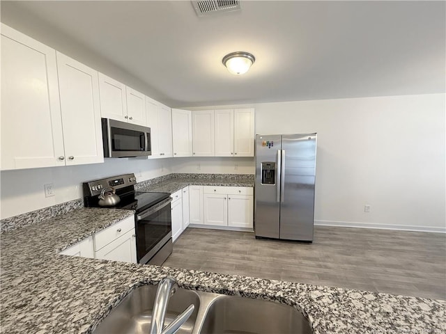 kitchen with sink, dark hardwood / wood-style flooring, dark stone countertops, white cabinets, and appliances with stainless steel finishes