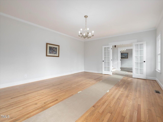 spare room with french doors, light hardwood / wood-style flooring, ornamental molding, and a notable chandelier