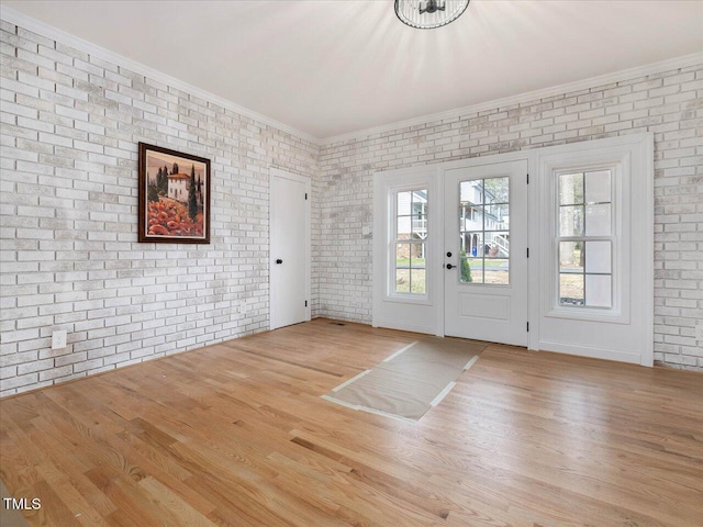 interior space with ornamental molding, brick wall, and light hardwood / wood-style flooring