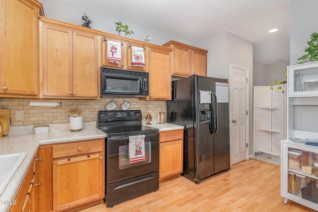 kitchen with tasteful backsplash, sink, black appliances, and light wood-type flooring