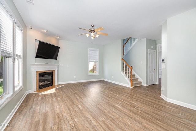 unfurnished living room featuring a fireplace, wood-type flooring, a healthy amount of sunlight, and ceiling fan