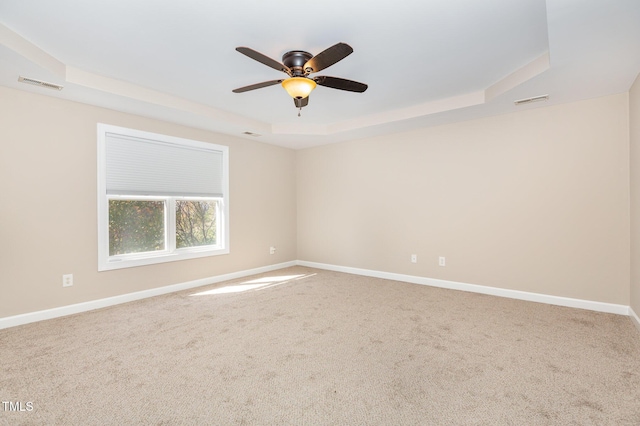 spare room with a raised ceiling, carpet, and ceiling fan