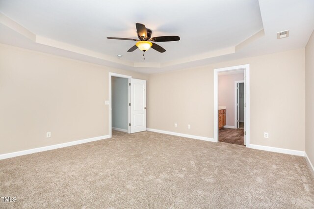 unfurnished bedroom with a tray ceiling, ensuite bathroom, ceiling fan, and carpet flooring