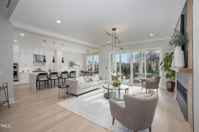 living room with light hardwood / wood-style floors, crown molding, and an inviting chandelier