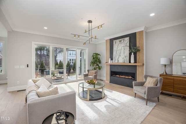 living room featuring a large fireplace, crown molding, a chandelier, and light wood-type flooring