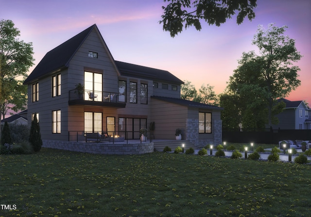 back house at dusk with a lawn and a balcony