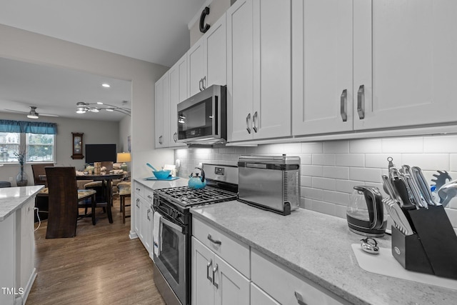 kitchen with white cabinets, decorative backsplash, light stone countertops, and stainless steel appliances