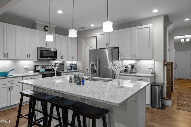 kitchen with pendant lighting, white cabinetry, stainless steel appliances, light stone counters, and a center island with sink