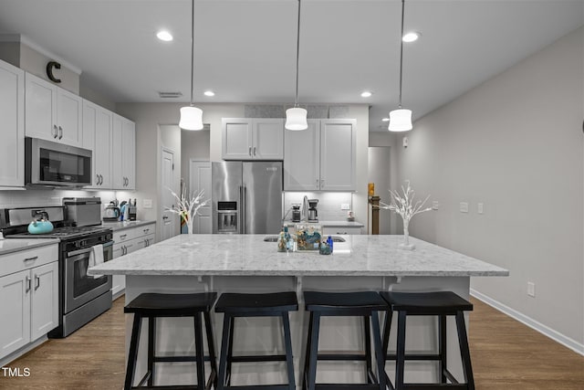 kitchen with decorative light fixtures, white cabinets, appliances with stainless steel finishes, and a center island with sink