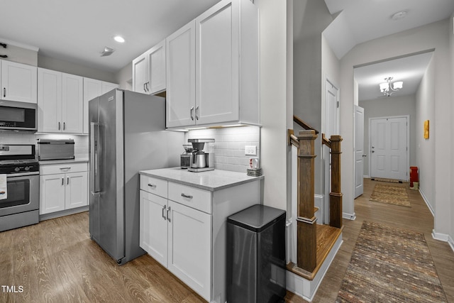 kitchen with light wood-type flooring, appliances with stainless steel finishes, backsplash, and white cabinets