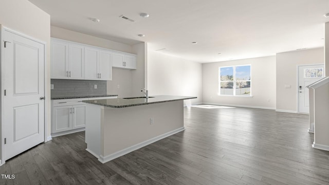 kitchen featuring white cabinets, dark hardwood / wood-style flooring, a center island with sink, and dark stone countertops