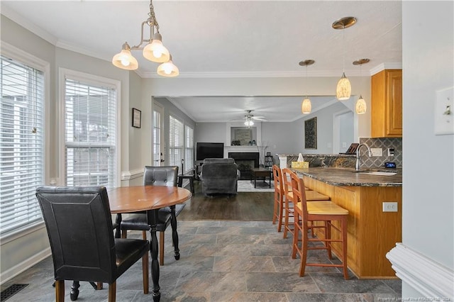 dining space featuring ceiling fan with notable chandelier, a healthy amount of sunlight, ornamental molding, and sink