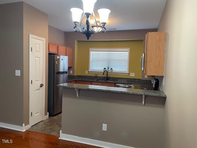 kitchen with sink, stainless steel appliances, a kitchen breakfast bar, kitchen peninsula, and dark stone counters