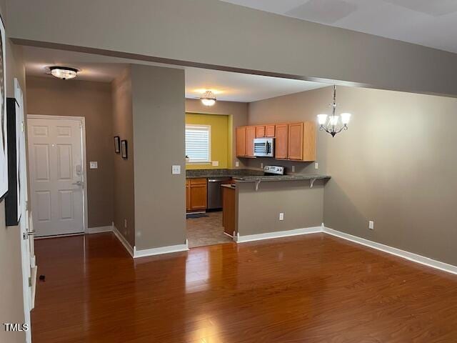 kitchen featuring a breakfast bar, dark hardwood / wood-style flooring, a chandelier, kitchen peninsula, and stainless steel appliances