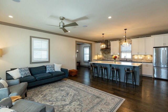 living room with dark wood-type flooring, ceiling fan, crown molding, and sink