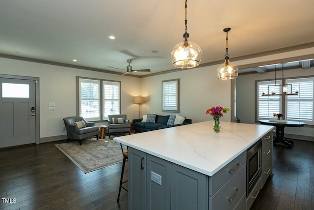 kitchen with stainless steel microwave, a center island, decorative light fixtures, dark hardwood / wood-style floors, and ceiling fan