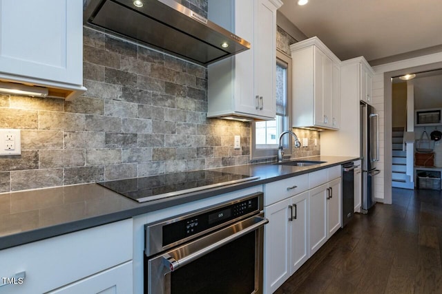 kitchen with wall chimney range hood, decorative backsplash, white cabinetry, appliances with stainless steel finishes, and sink