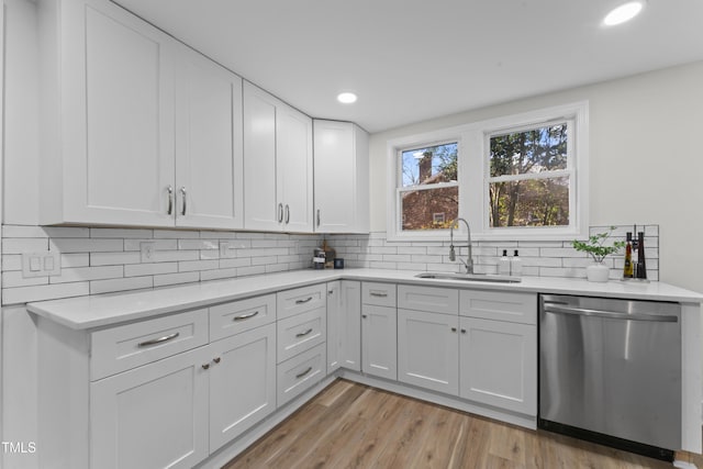 kitchen featuring dishwasher, sink, light hardwood / wood-style floors, decorative backsplash, and white cabinets