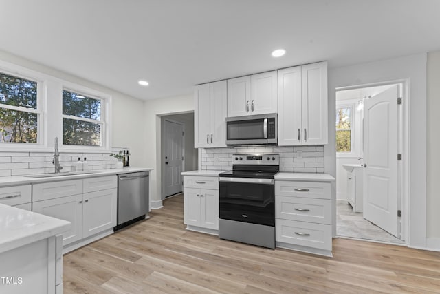 kitchen featuring decorative backsplash, light wood-type flooring, stainless steel appliances, sink, and white cabinets