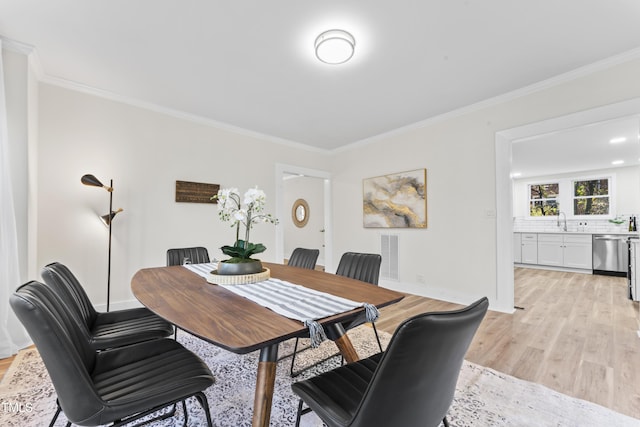 dining room featuring sink, light wood-type flooring, and ornamental molding