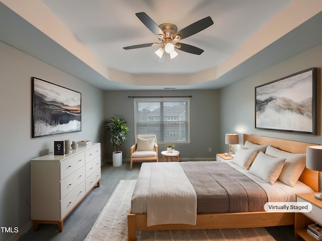 bedroom featuring a raised ceiling, ceiling fan, and dark colored carpet