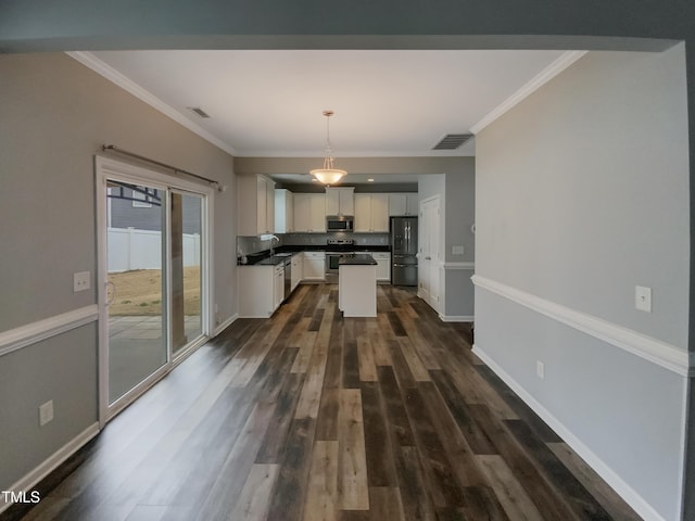 kitchen featuring ornamental molding, stainless steel appliances, dark wood-type flooring, pendant lighting, and white cabinetry