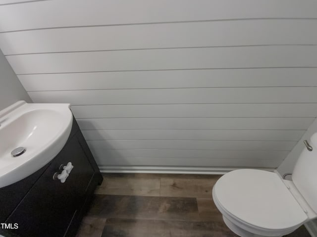 bathroom with hardwood / wood-style floors, vanity, toilet, and wooden walls