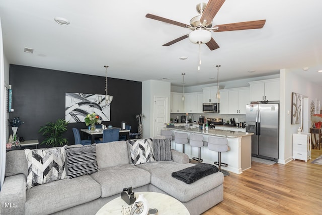 living room with ceiling fan with notable chandelier and light hardwood / wood-style floors