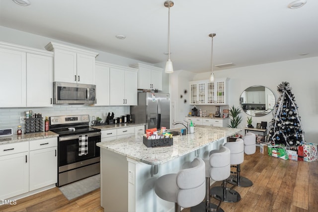 kitchen with stainless steel appliances, hanging light fixtures, a center island with sink, and white cabinets