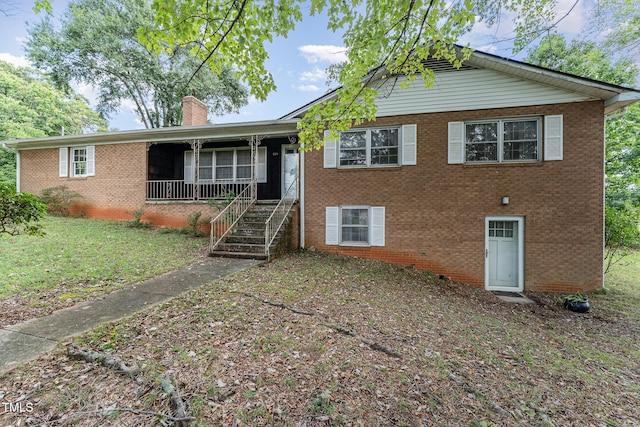 view of front of property featuring brick siding, a chimney, a porch, and a front lawn