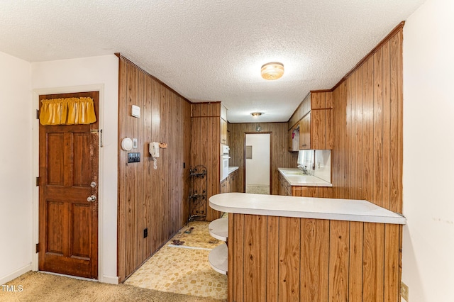 kitchen with a textured ceiling, light colored carpet, a sink, light countertops, and brown cabinets