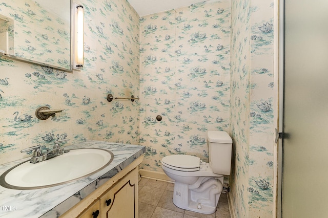 bathroom featuring toilet, vanity, baseboards, tile patterned floors, and wallpapered walls