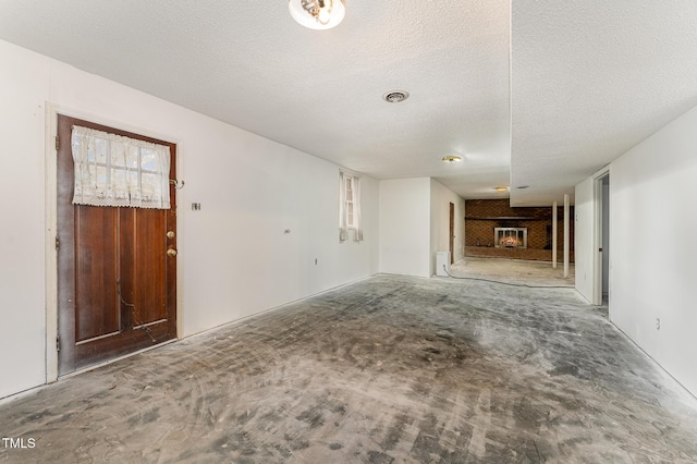 unfurnished living room with a textured ceiling, a brick fireplace, and visible vents