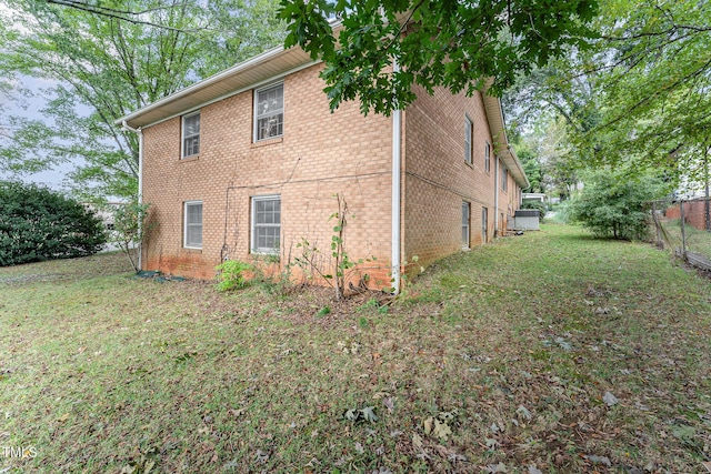 view of property exterior featuring brick siding, a lawn, and fence