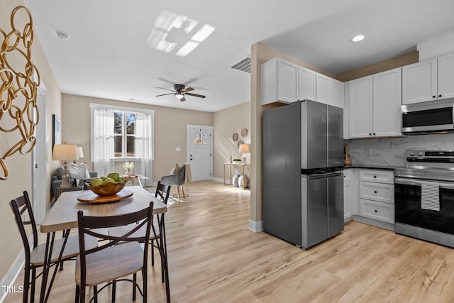 kitchen with stainless steel appliances, light wood-type flooring, white cabinets, and backsplash