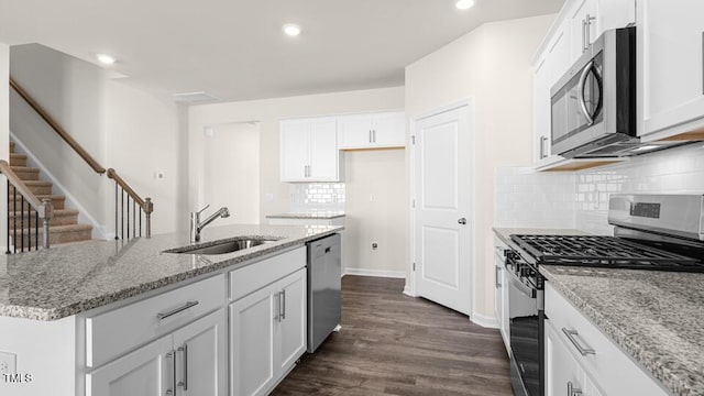 kitchen with light stone countertops, stainless steel appliances, dark wood-style floors, white cabinetry, and a sink