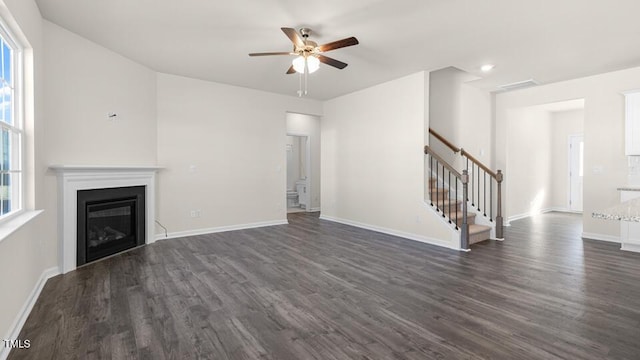 unfurnished living room featuring a glass covered fireplace, baseboards, dark wood-style floors, and stairs