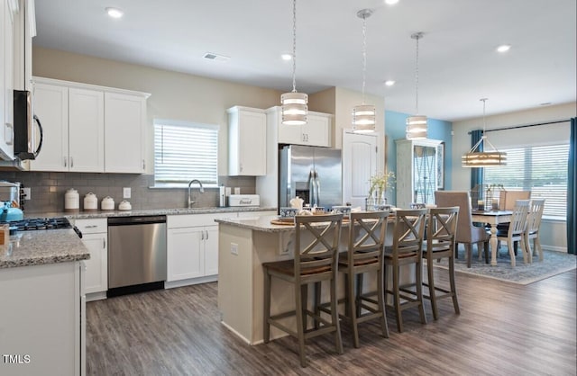 kitchen featuring white cabinetry, stainless steel appliances, tasteful backsplash, pendant lighting, and a kitchen island