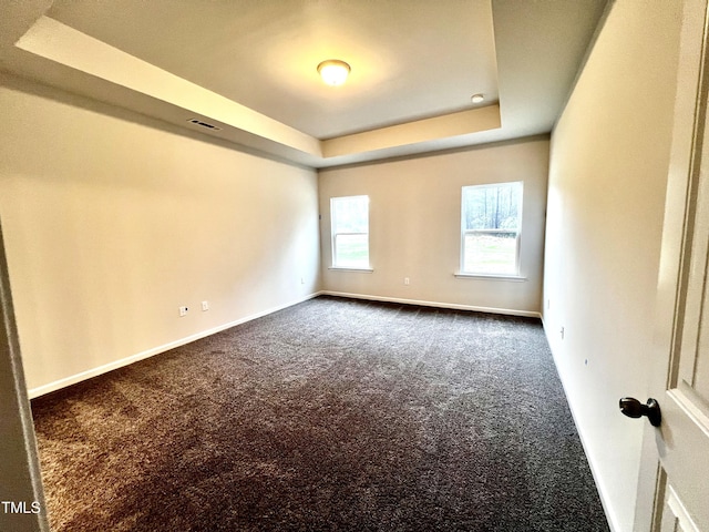 spare room featuring dark colored carpet, baseboards, a raised ceiling, and visible vents