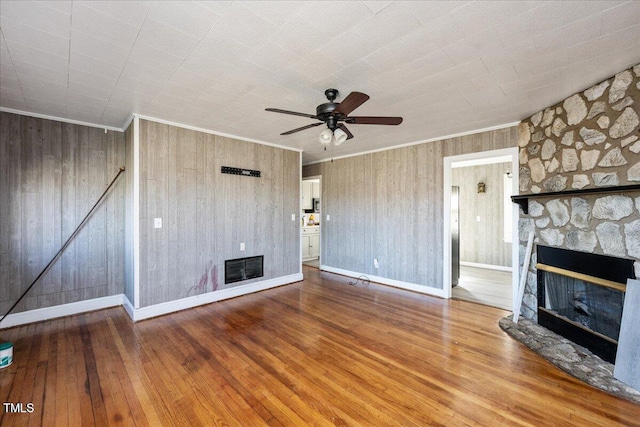 unfurnished living room featuring ornamental molding, ceiling fan, wooden walls, a fireplace, and hardwood / wood-style floors